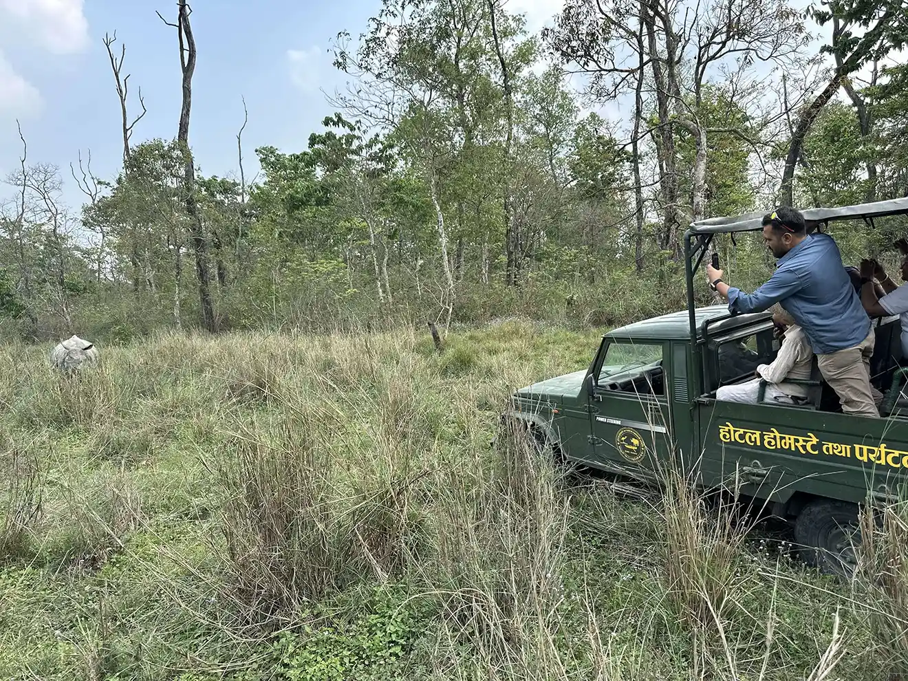 Travelers on a jungle safari jeep observe a one-horned rhinoceros in the tall grass, highlighting outdoor adventures near the best cities to visit in Nepal.