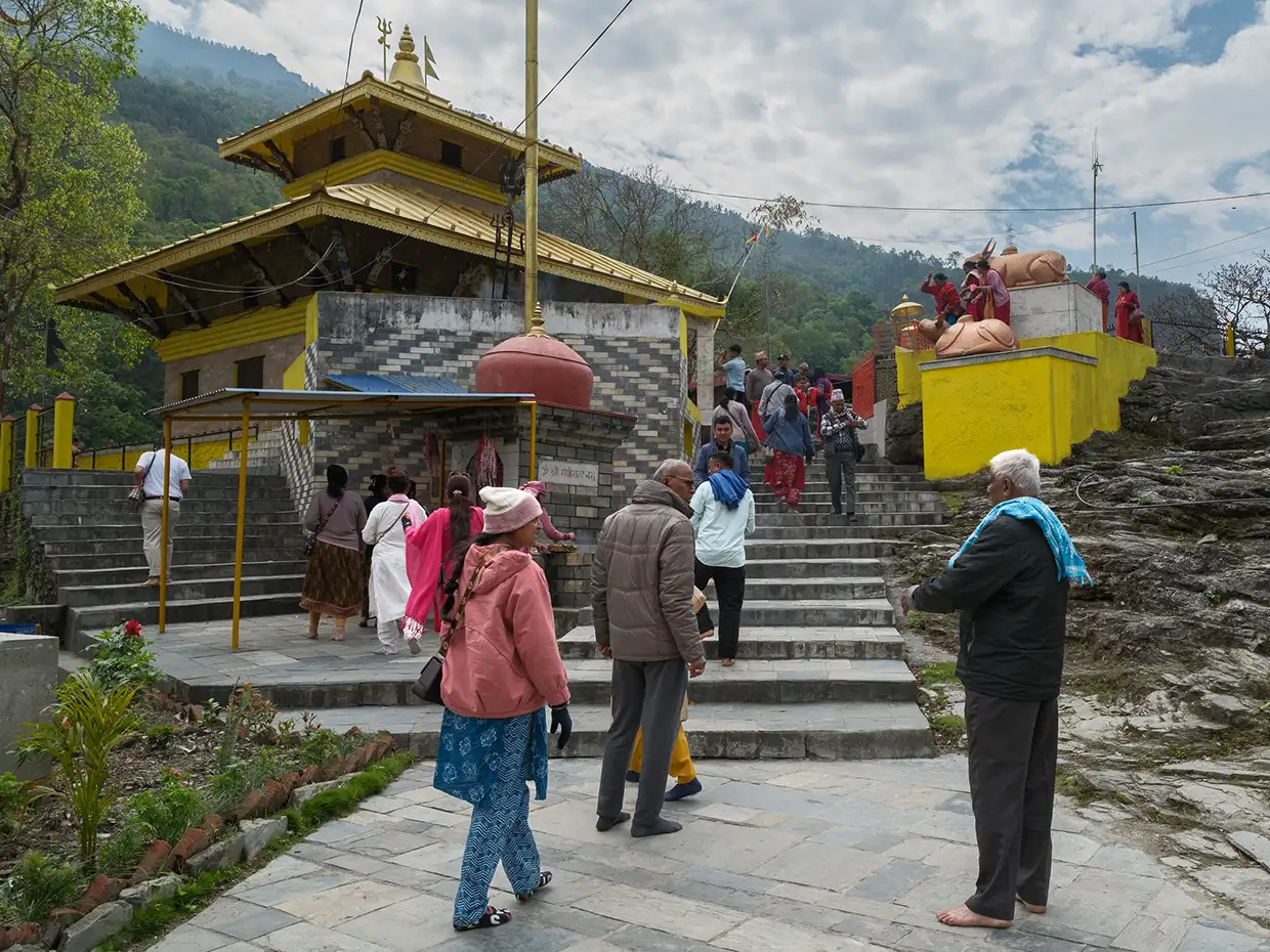 An ornate stone archway leads into the historic Galeshwor Temple complex, set against steep, lush green mountainsides along the Annapurna Community Trek.