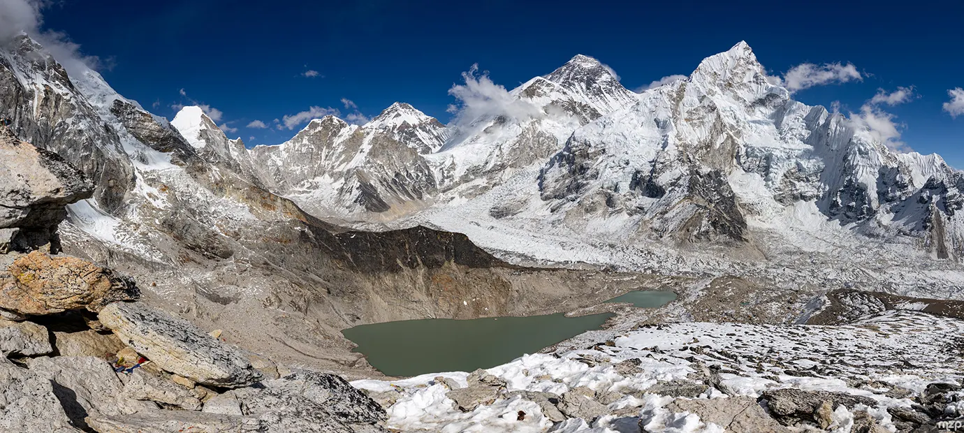 A sweeping mountain panorama shows snow-covered Himalayan peaks above a turquoise glacial lake. This Everest Panorama Trek Guide helps travelers plan their journey through this rugged landscape.