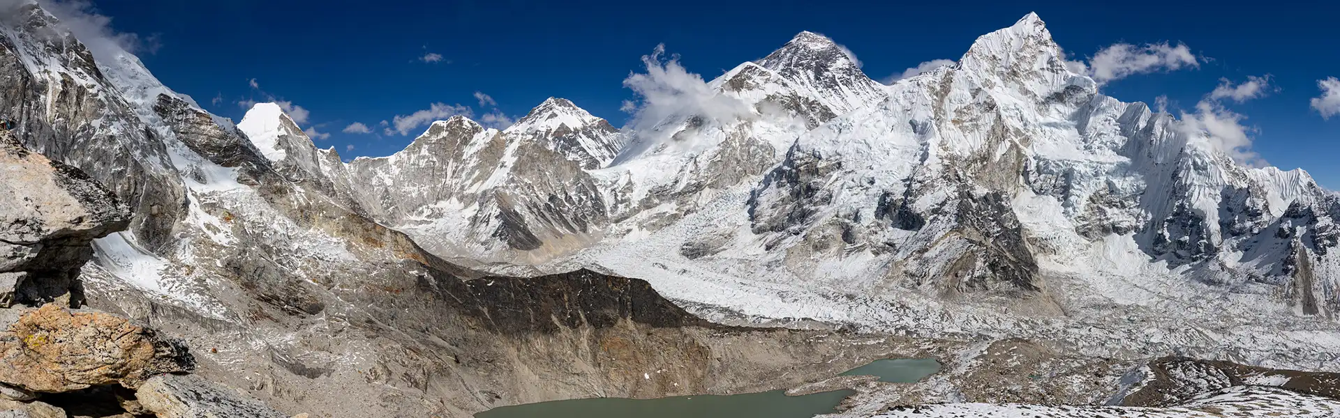 A wide panoramic view shows the massive snow-covered peaks and glacial valleys of the Himalayas under a blue sky. Proper Fitness Training for Everest Base Camp trek helps travelers enjoy these views.