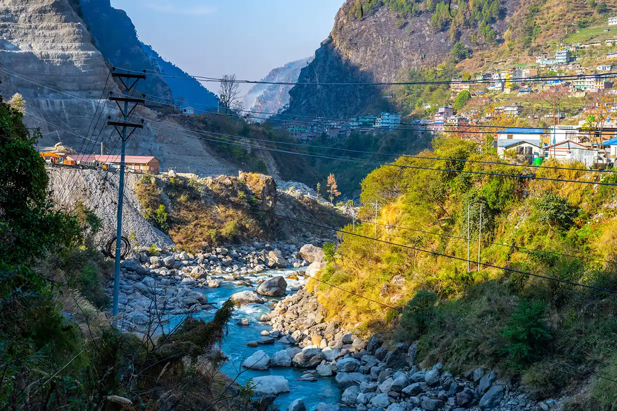 A rocky blue river flows through a steep mountain gorge toward the bustling hillside town of Syabrubesi, the traditional starting point for a Tamang Heritage Trek.