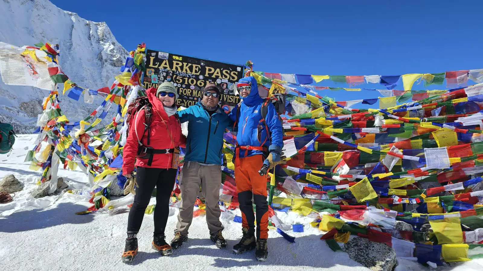 Trekkers celebrate at Larkya Pass on the Manaslu Circuit, surrounded by prayer flags, snow-covered terrain, and clear Himalayan mountain views.