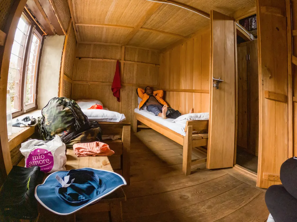 A traveler rests on a simple wooden bed inside a cozy, wood-paneled tea house room during the Khopra Ridge Trek in Nepal.