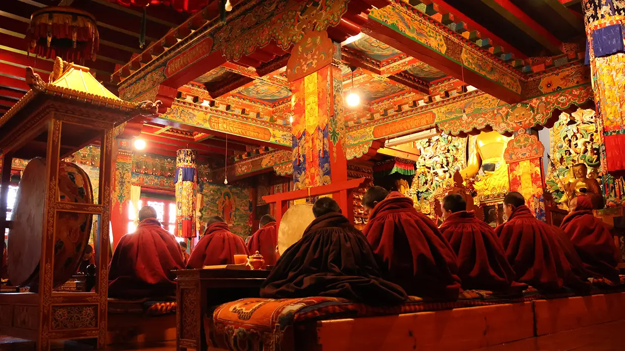 Buddhist monks in maroon robes sit in prayer inside a beautifully painted, ornate monastery hall during the Everest Cultural Trek in Nepal.