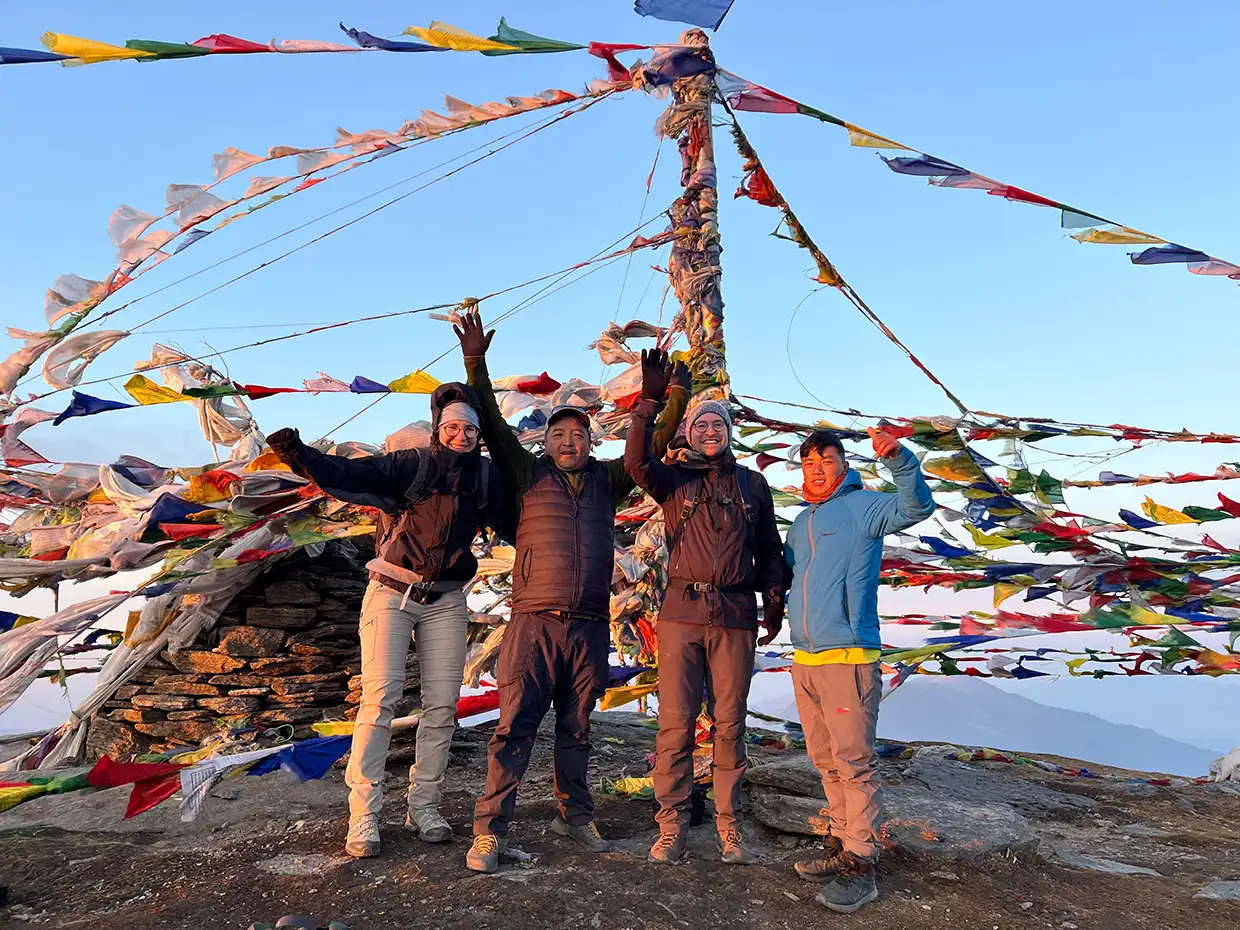 Four happy hikers stand together and raise their arms in celebration at a rocky summit covered in colorful prayer flags during a Pikey Peak Trek.