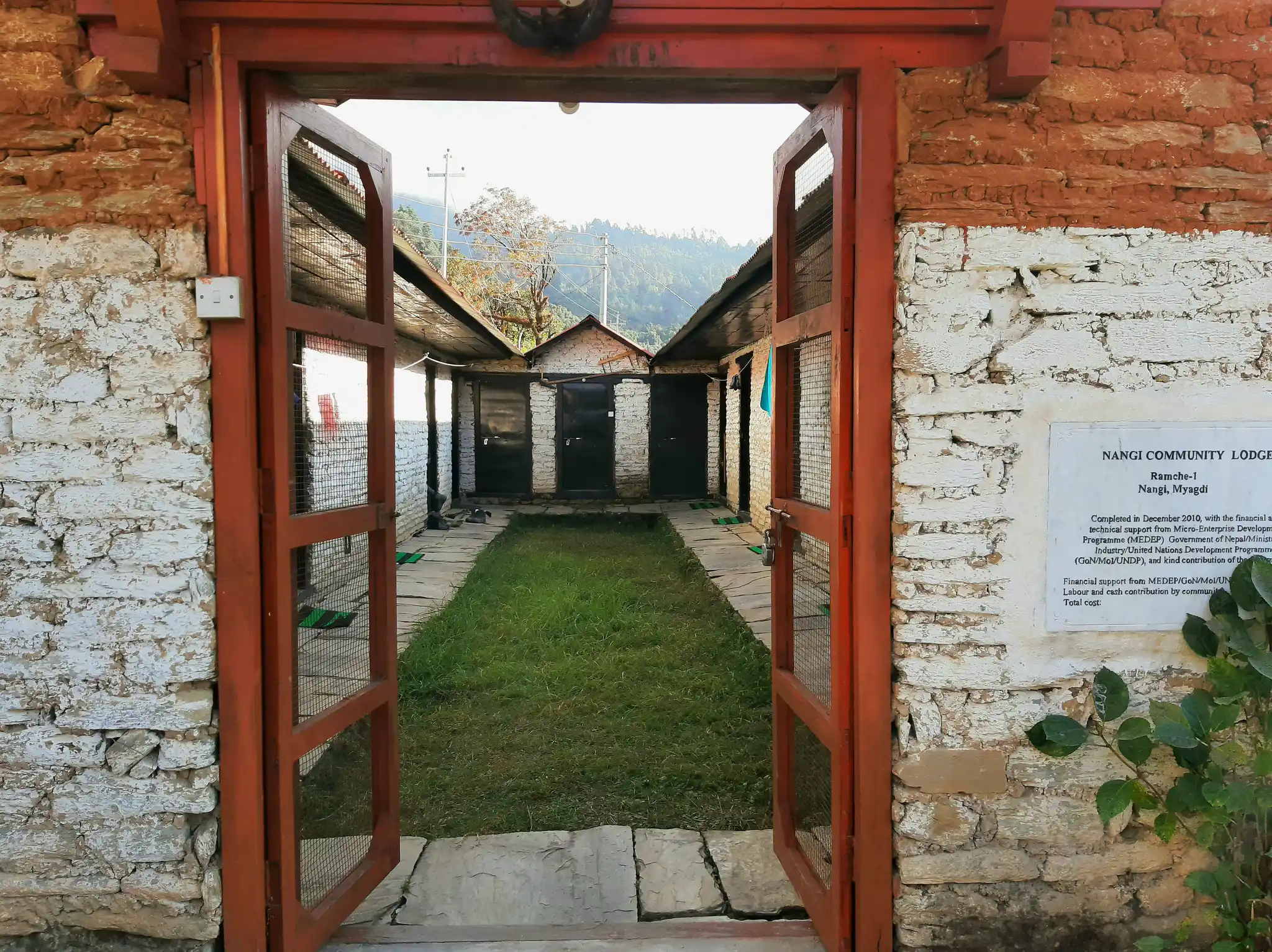 Open wooden doors reveal the grassy courtyard of Nangi Community Lodge, a rustic stone accommodation along the Annapurna Community Trek.