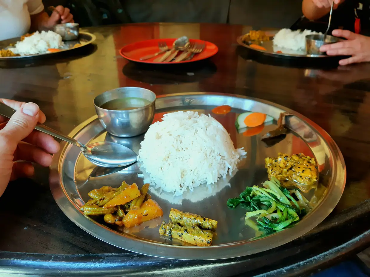 A traditional Nepalese Dal Bhat meal featuring rice, lentil soup, and vegetable side dishes is served on metal platters during the Annapurna Community Trek.