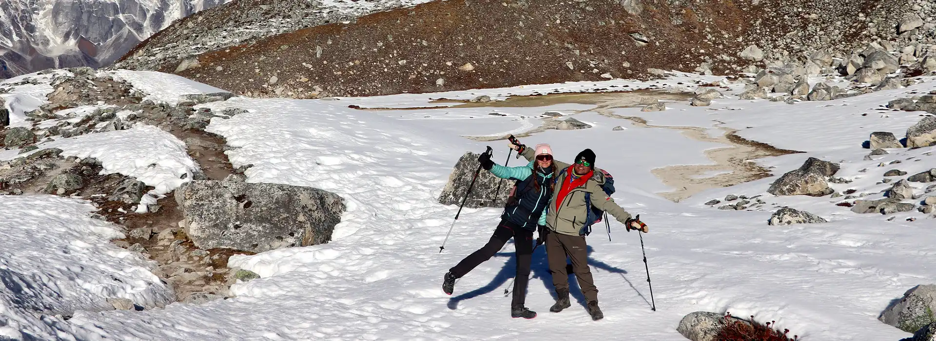 Two happy trekkers strike a playful pose with their trekking poles on a snowy mountain pass, an exciting moment highlighted in our Manaslu Circuit Trek Guide.