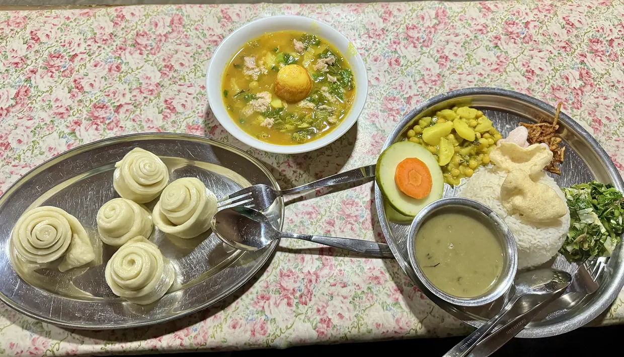 A traditional meal featuring dal bhat, soup with meat and eggs, and rolled steamed buns rests on a table, highlighting culinary insights from a Manaslu Circuit Trek Cost
