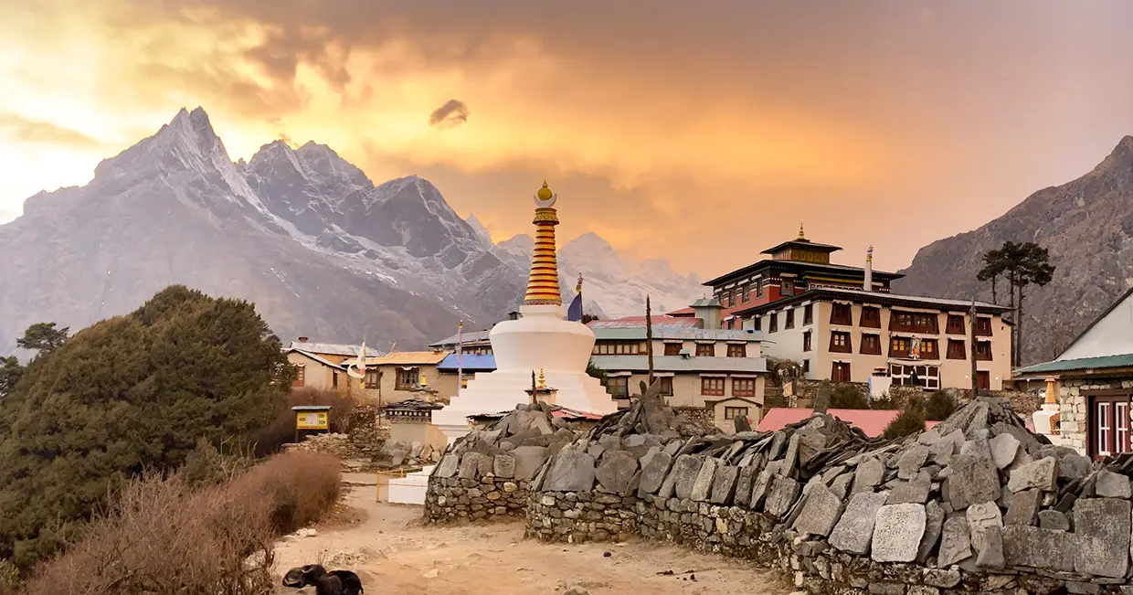 A white Buddhist stupa stands before Tengboche Monastery during sunset on an Everest Cultural Trek, with snow-covered Himalayan peaks under a golden sky.