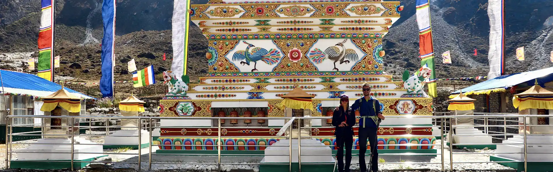 Two trekkers stand before a colorful Buddhist chorten adorned with traditional paintings and prayer wheels. A complete Manaslu Trek Packing Guide prepares travelers for these cultural sites.