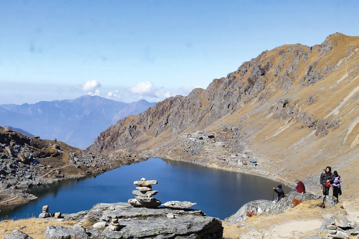 Hikers sit near a stone cairn overlooking the blue waters of Khayer Lake along the Khopra Ridge Trek in the Annapurna region.