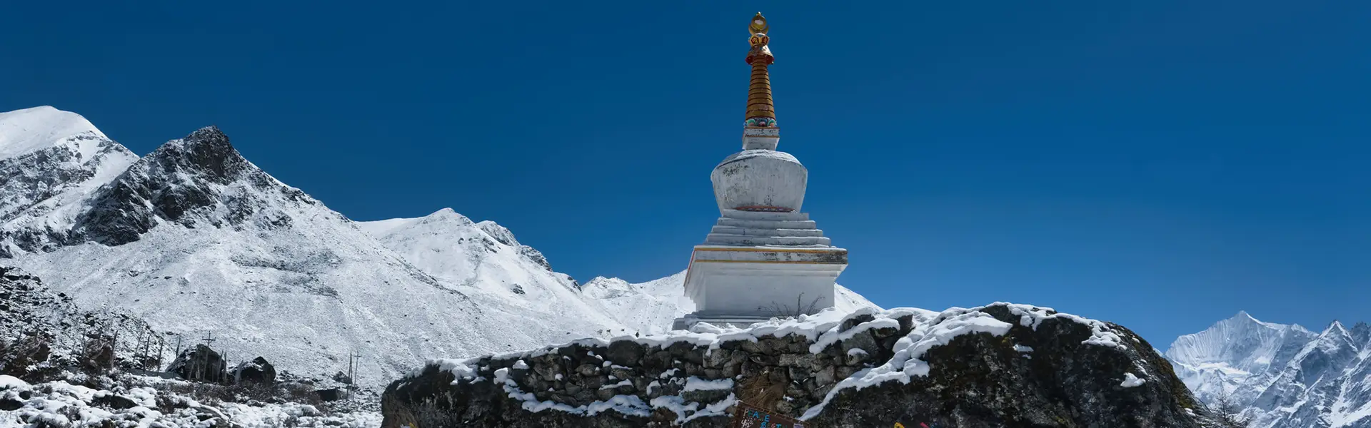 A white Buddhist stupa stands against a deep blue sky and snow-capped peaks, a scenic landmark detailed in our Langtang Valley Trek Guide.