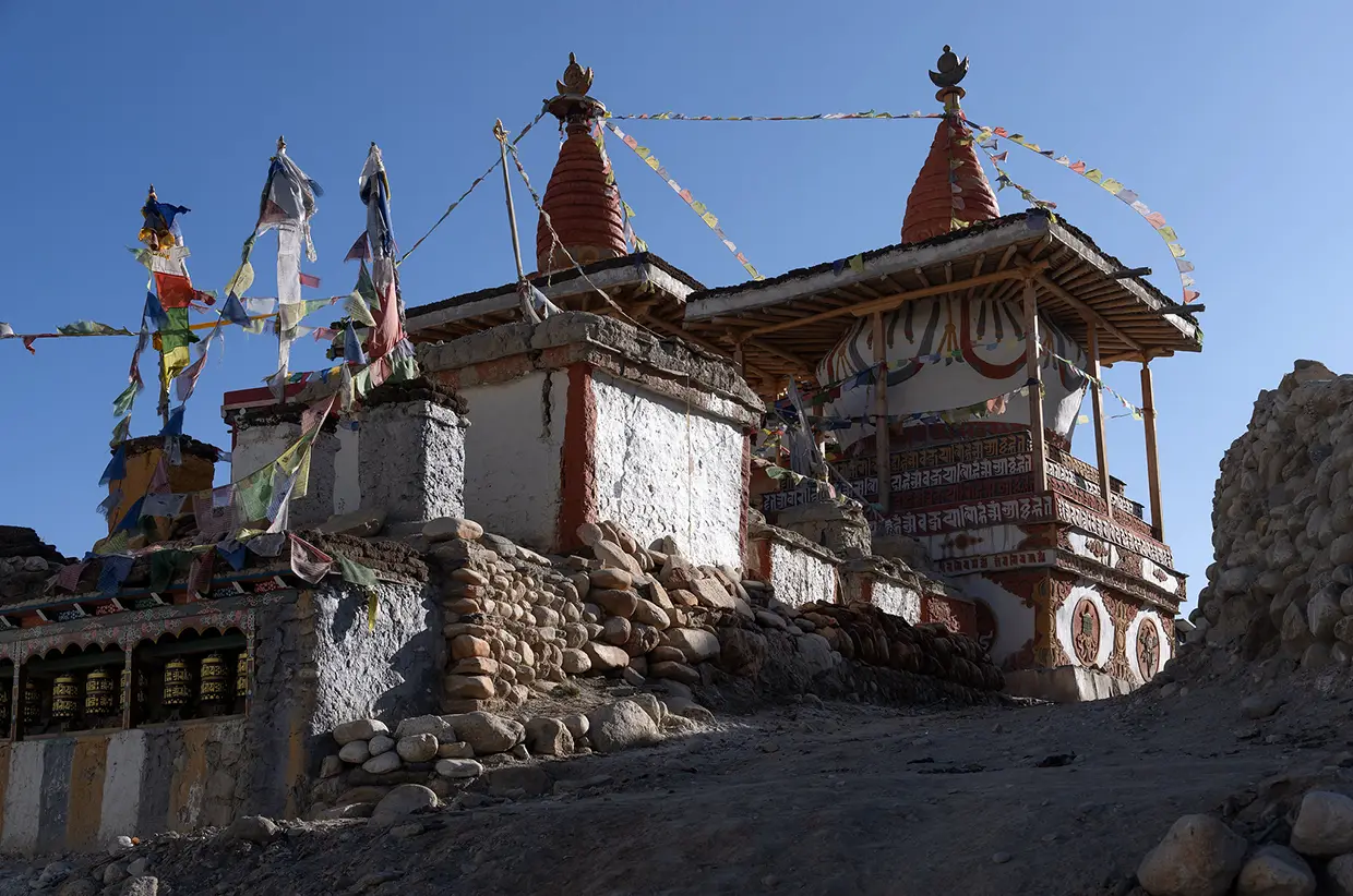 Ancient stone stupas with colorful prayer flags stand against a blue sky in Lo Manthang. Following Nepal Trekking Regulations helps protect these historic sites and your travel experience.