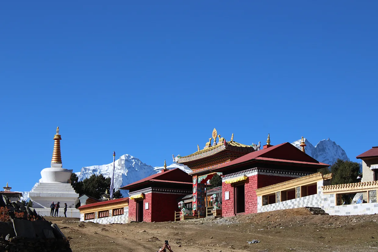 Trekkers stand near a white stupa and the red entrance gate of Tengboche Monastery under a clear sky on an Everest Cultural Trek.