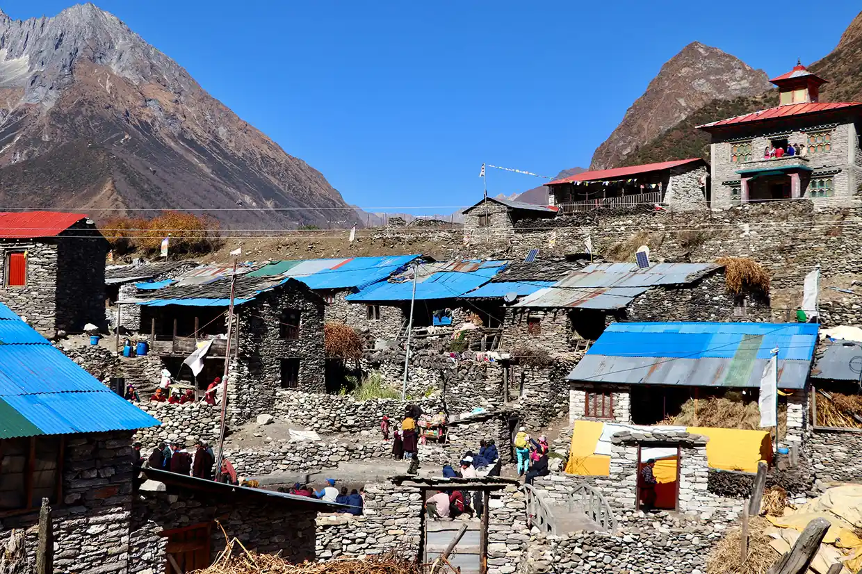 Stone houses with blue and red roofs sit nestled in a mountain valley. Understanding the Manaslu Circuit Trek Difficulty helps travelers prepare for these remote villages.