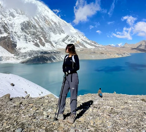 A hiker stands with a trekking pole overlooking the vibrant blue waters and snow-covered peaks during the Annapurna Circuit with Tilicho Lake Trek.