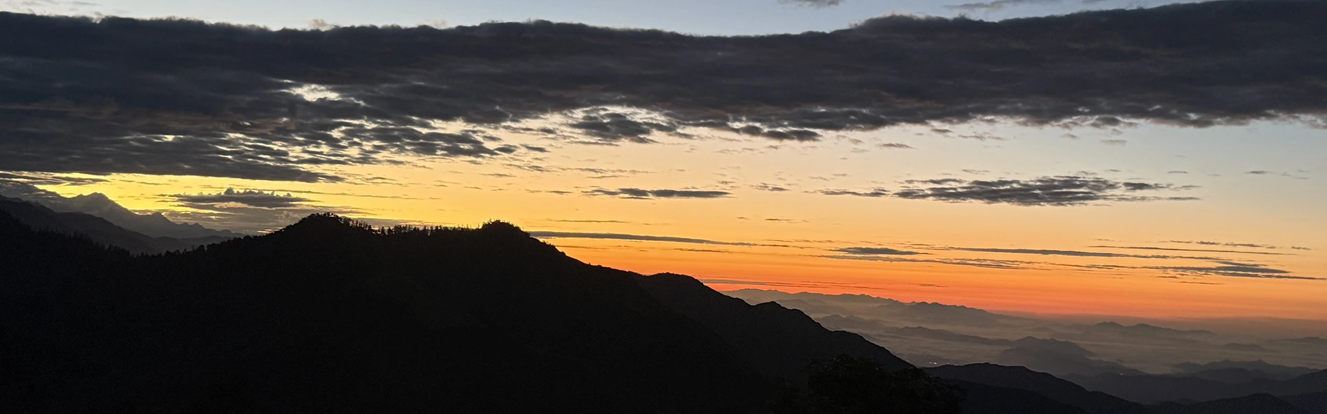 The sun rises over dark mountain silhouettes, painting the sky in vibrant orange and yellow hues. This Poon Hill Trek Guide helps you find the best morning views.