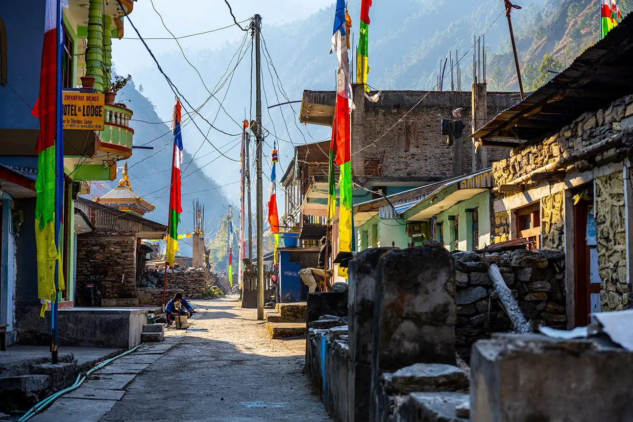 Colorful prayer flags line a narrow stone street in Syabrubesi, the bustling gateway village where most travelers begin their Langtang Trek Itinerary in Nepal.