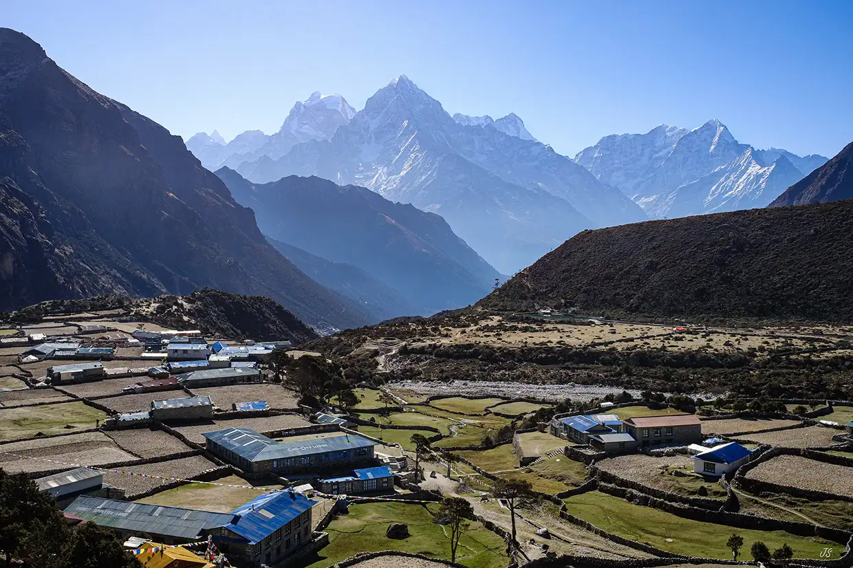 A scenic view of Thame village with stone houses and blue roofs against majestic mountain peaks during an Everest Cultural Trek in Nepal.