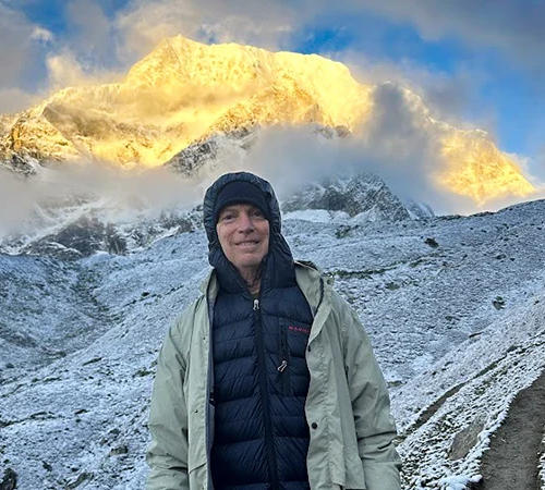 A smiling trekker in a hooded down jacket stands on a snowy trail. Following a Manaslu Trek Packing Guide ensures you have warm layers for golden mountain sunrises.