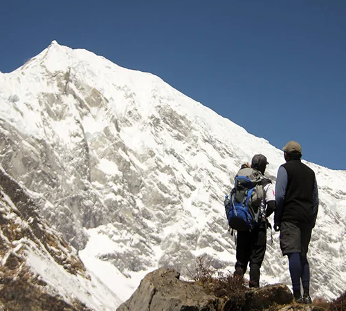 Two hikers with backpacks stand on a rocky outcrop, admiring a massive snow-covered Himalayan peak as described in our Langtang Gosaikunda Trek Guide.