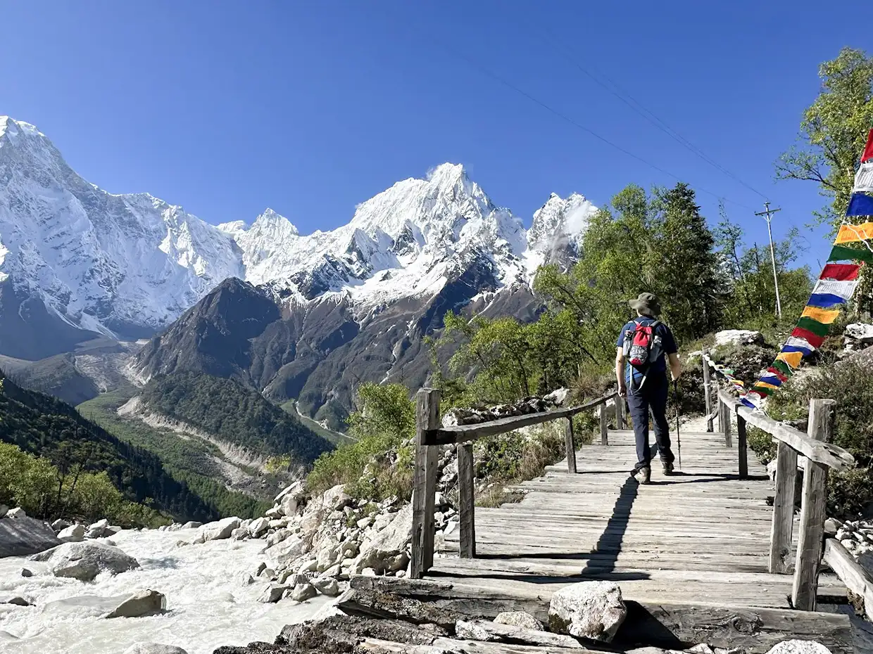A trekker crosses a wooden bridge over a rushing river in Nepal. The Manaslu Trek Permit Guide helps travelers reach these snow-capped mountain vistas safely.