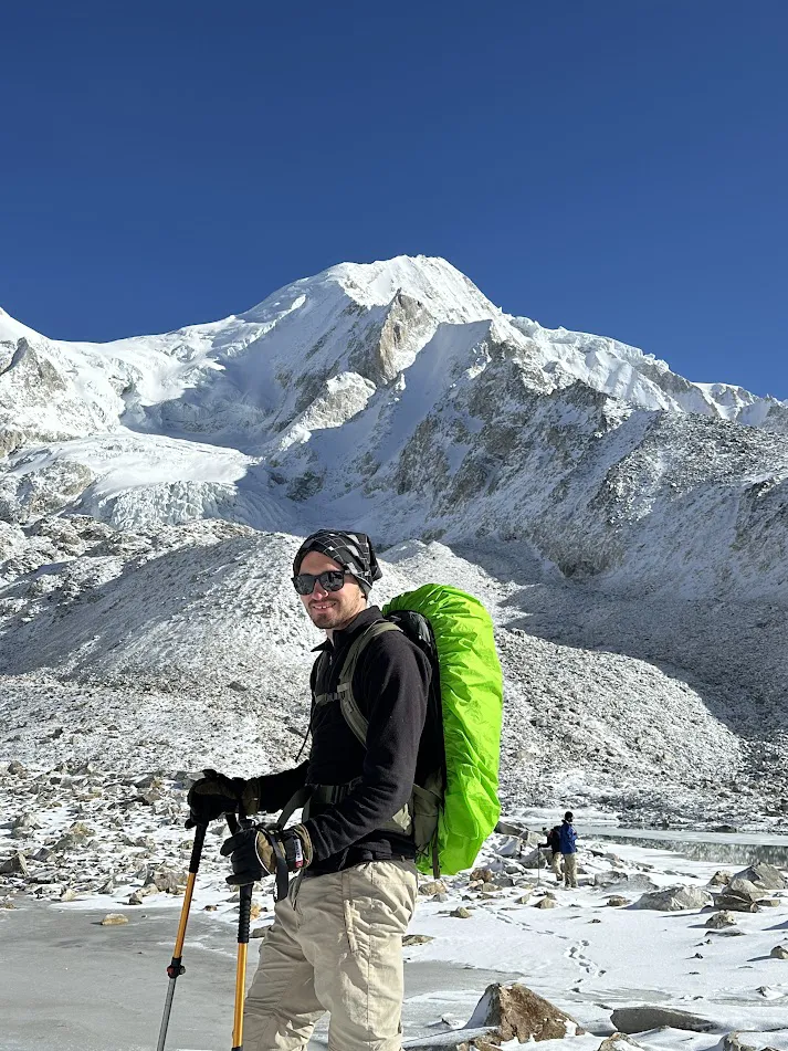 A traveler with a backpack stands among yellow tents at the Dharmasala campsite below a brown, rocky mountain, a helpful visual for a Manaslu Trek Permit Guide.