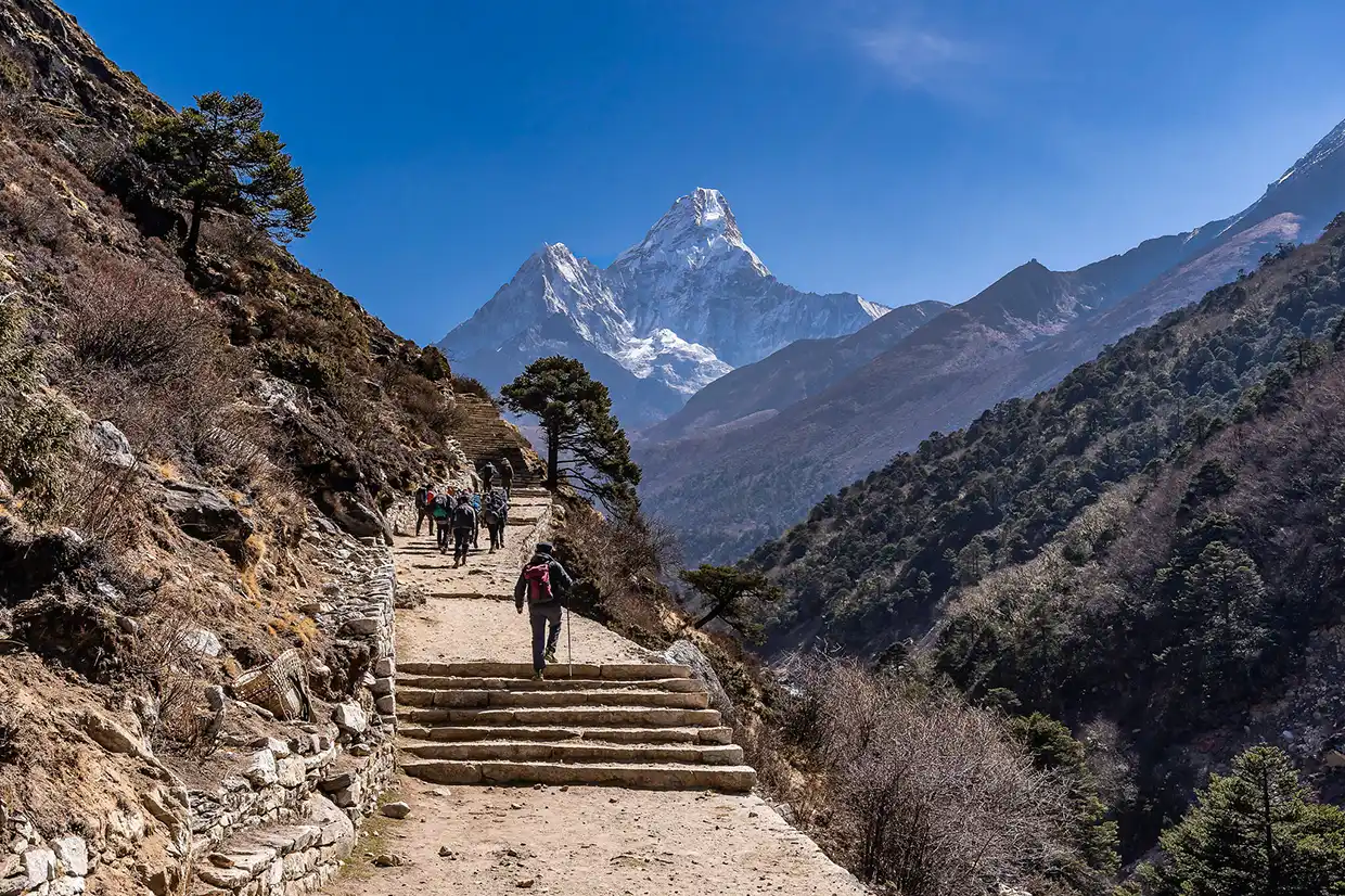 A group of trekkers climbs a stone path toward the iconic Ama Dablam peak under a clear blue sky, illustrating the adventure described in this Everest Base Camp Trek Guide.