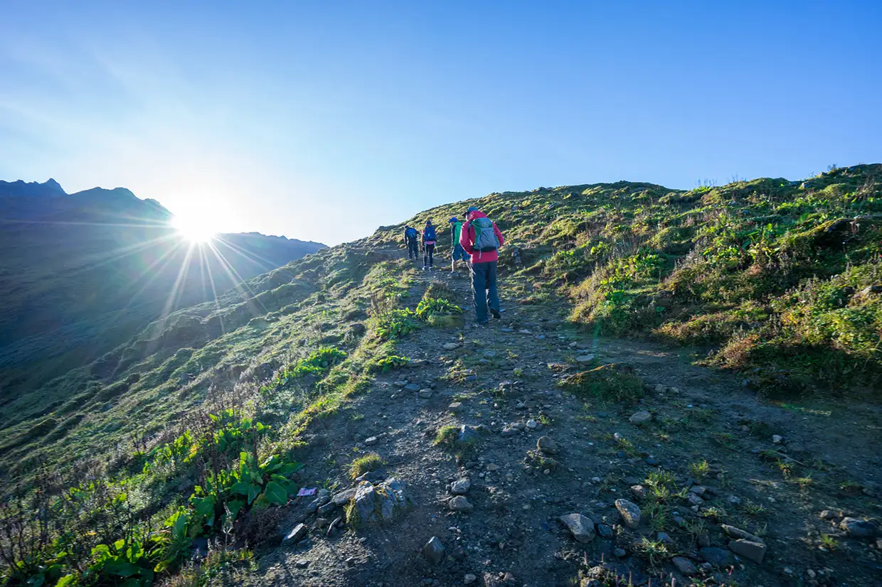 A group of hikers ascends a rocky mountain trail under a bright sun during the scenic Khopra Ridge Trek in Nepal.
