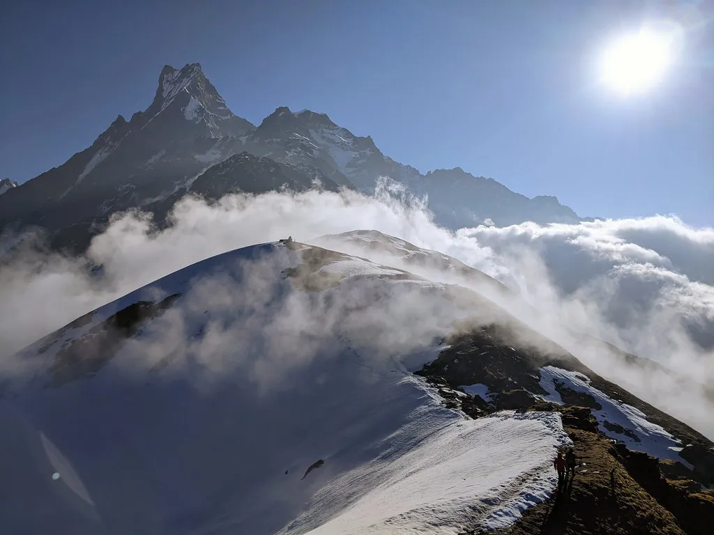 Snowy mountain ridges peak through a thick blanket of white clouds under a bright sun. This Mardi Himal Trek Guide helps you navigate these high-altitude landscapes safely.