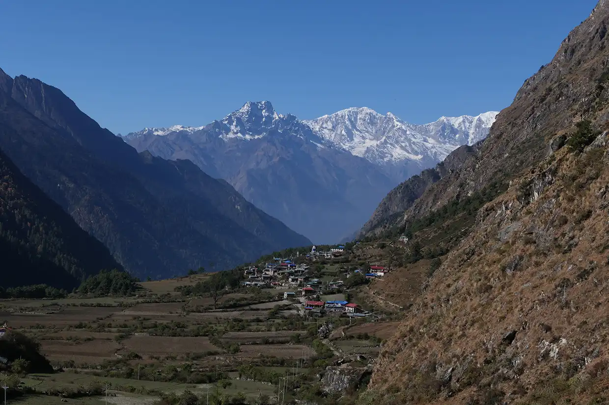 A remote mountain settlement sits in a wide valley beneath towering snow-capped peaks in Chhokangparo village.webp along the Manaslu Tsum Valley Trek.