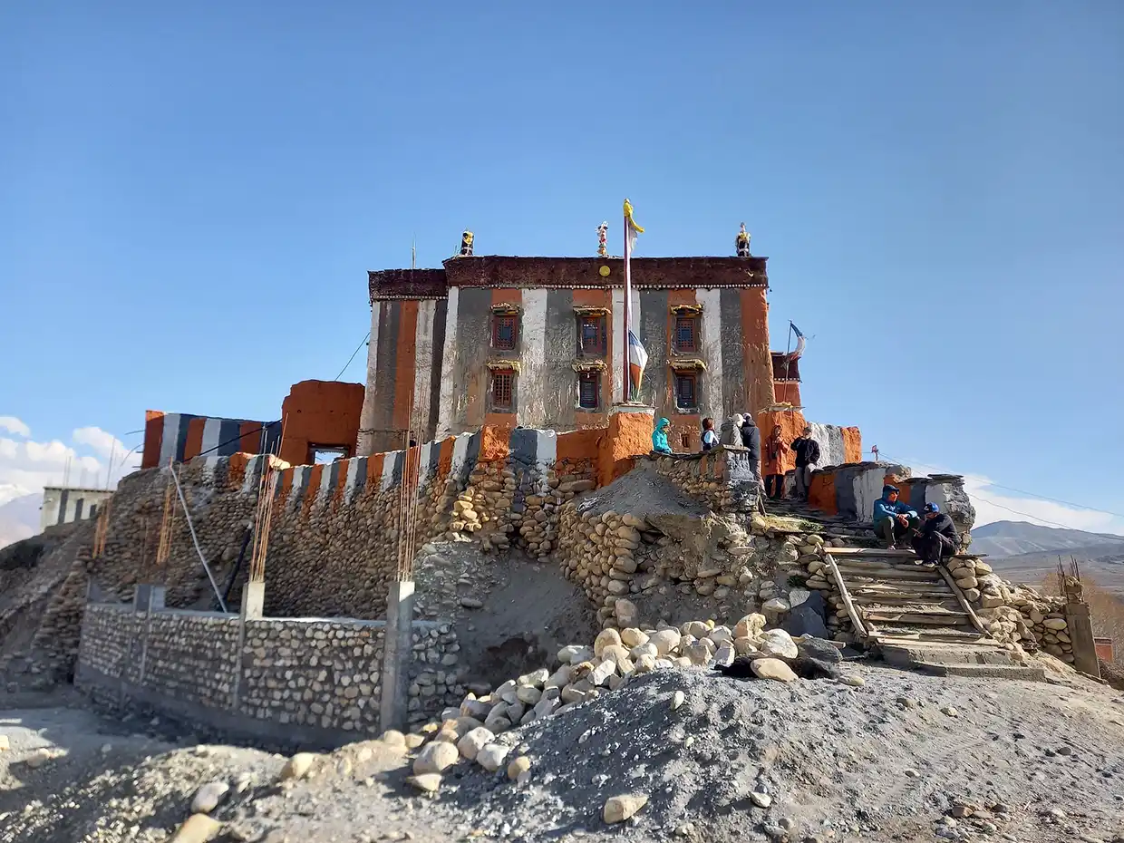 Travelers rest outside a traditional red and white Buddhist monastery built on a stone hill during a luxury Upper Mustang Jeep Tour in Nepal.
