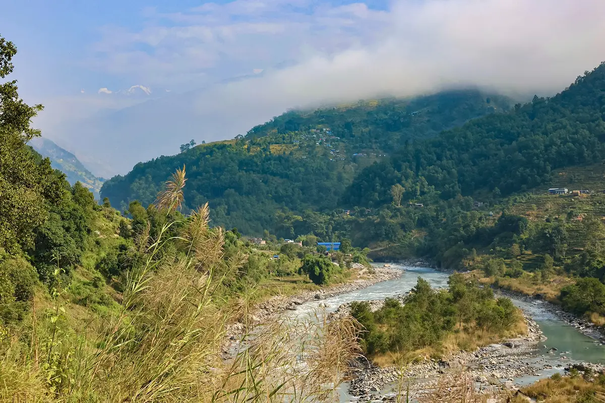 The Budhi Gandaki River winds through a lush green valley under low clouds along the scenic Manaslu Tsum Valley Trek trail in Nepal.