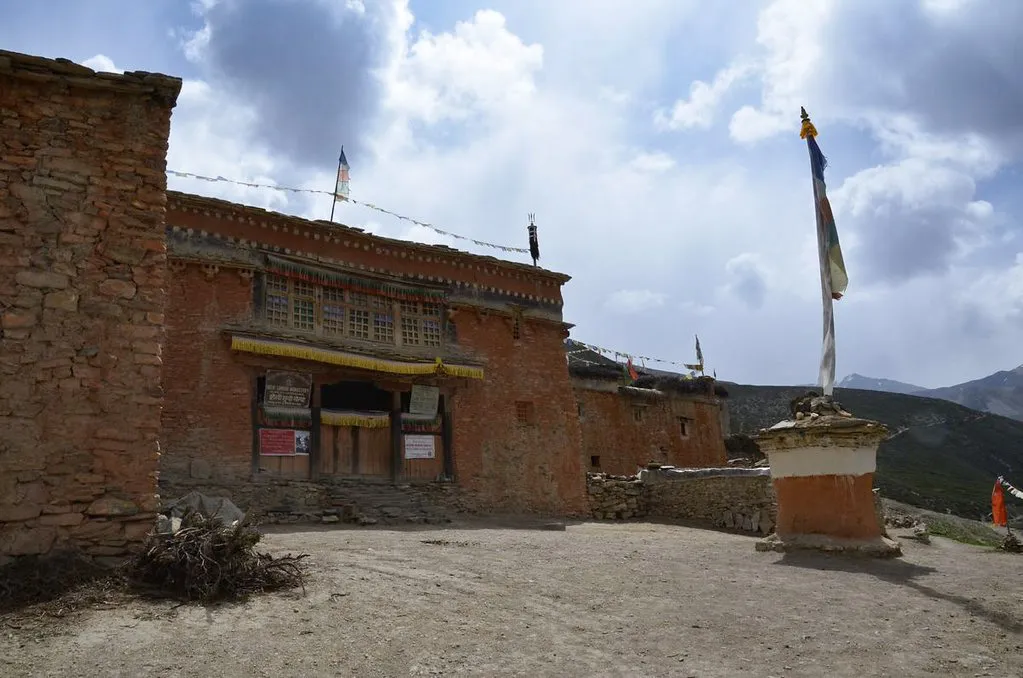 An ancient red stone monastery stands in a high mountain valley under a cloudy sky, a key cultural highlight along the Upper Dolpo Trek.