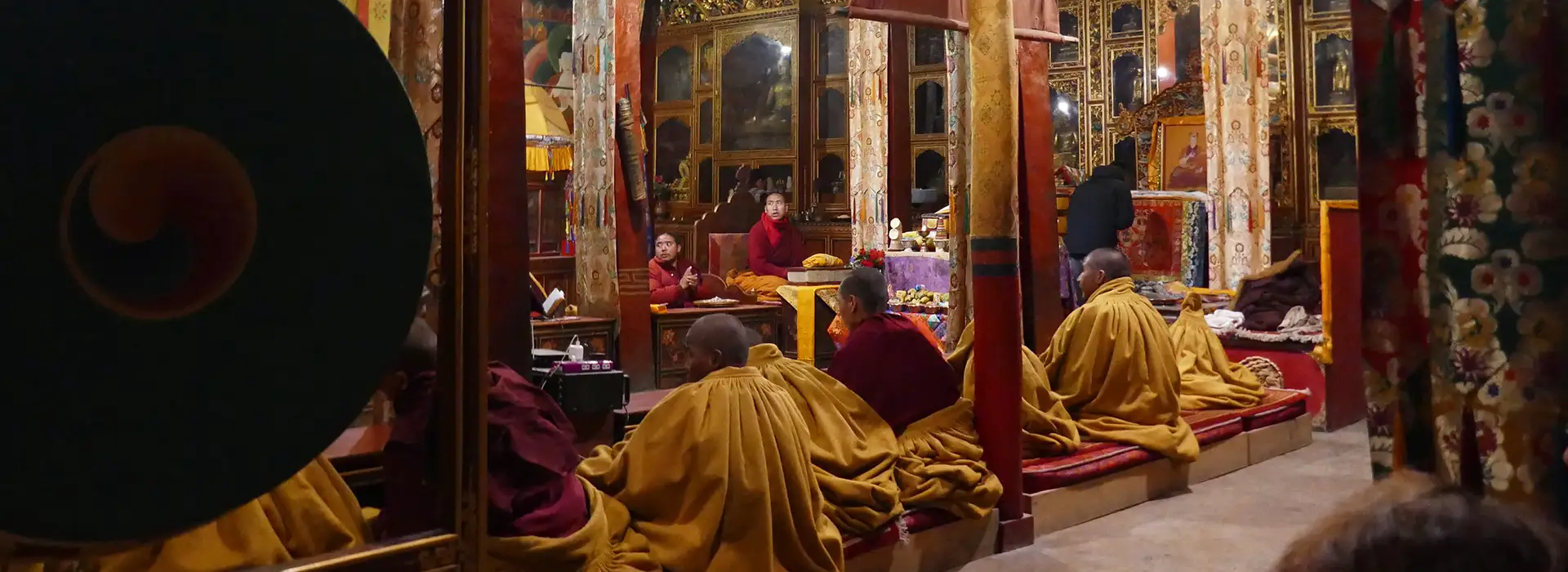 Buddhist monks gather inside a dimly lit ornate monastery for prayer during a culturally immersive Upper Mustang Jeep Tour in Nepal.
