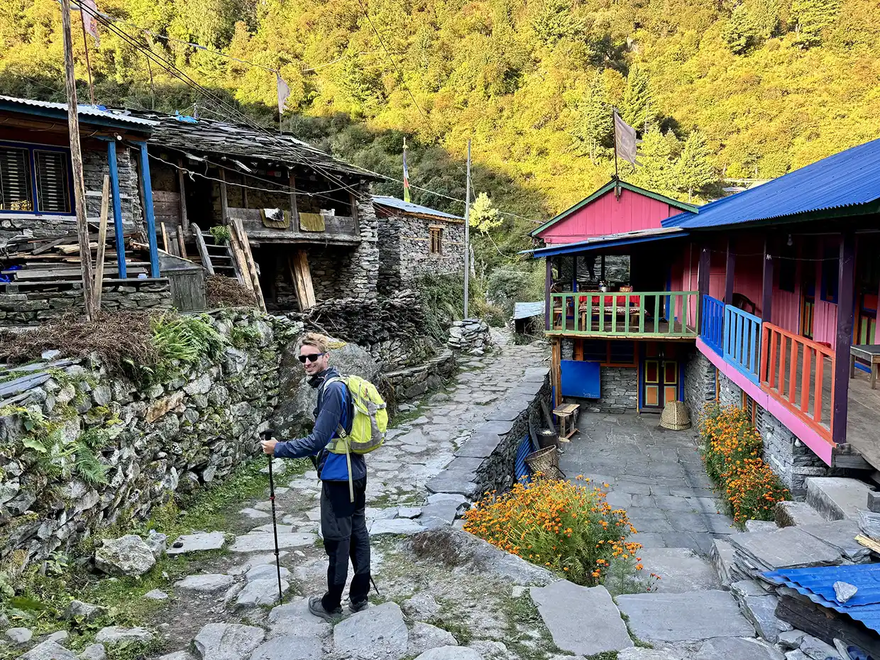 A hiker with a backpack stands on a stone path between traditional houses during the Manaslu Tsum Valley Trek in Nepal.