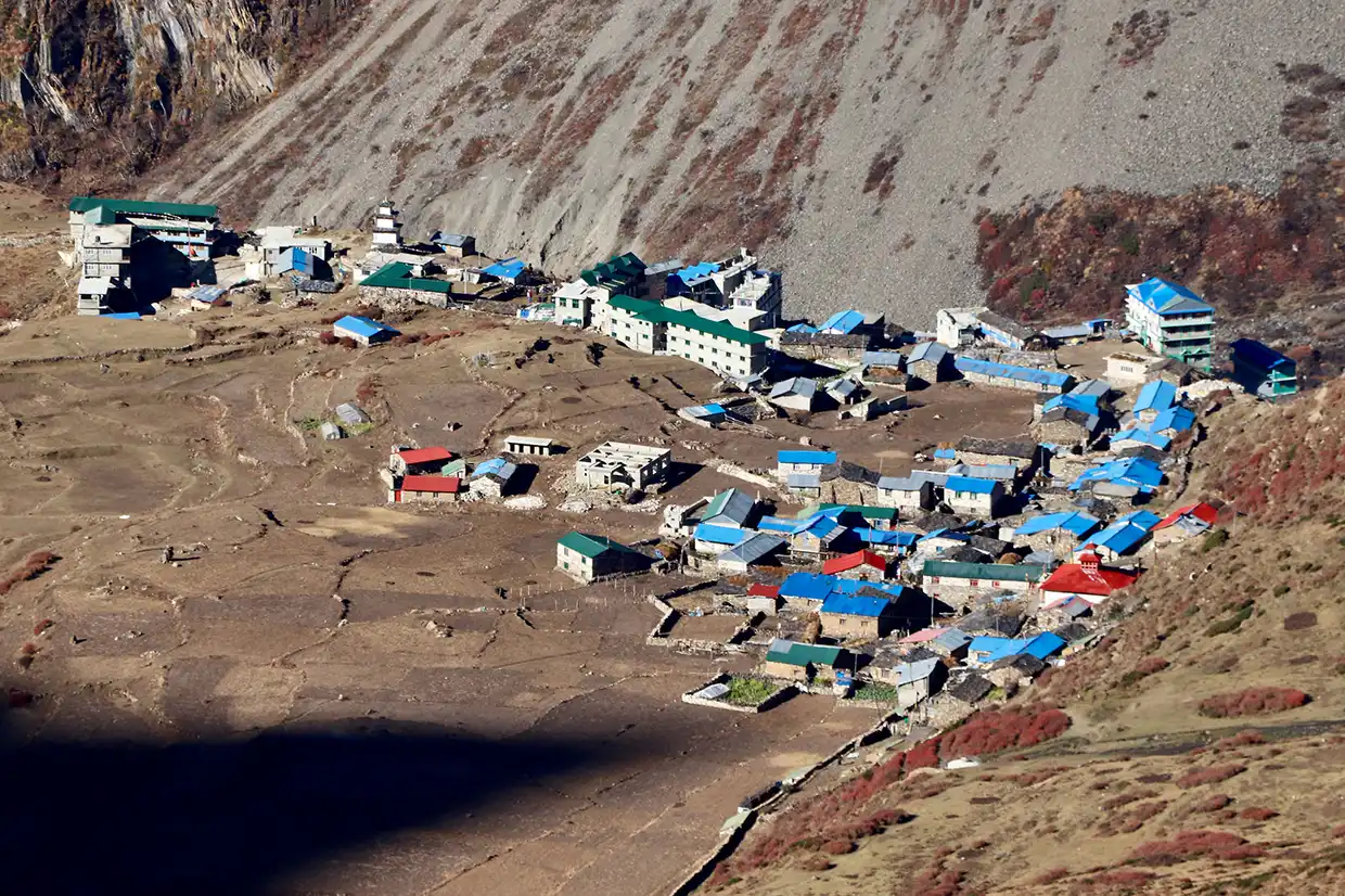 An aerial view of a rustic mountain village with colorful roofs and stone buildings tucked under a steep slope on the Manaslu Tsum Valley Trek.