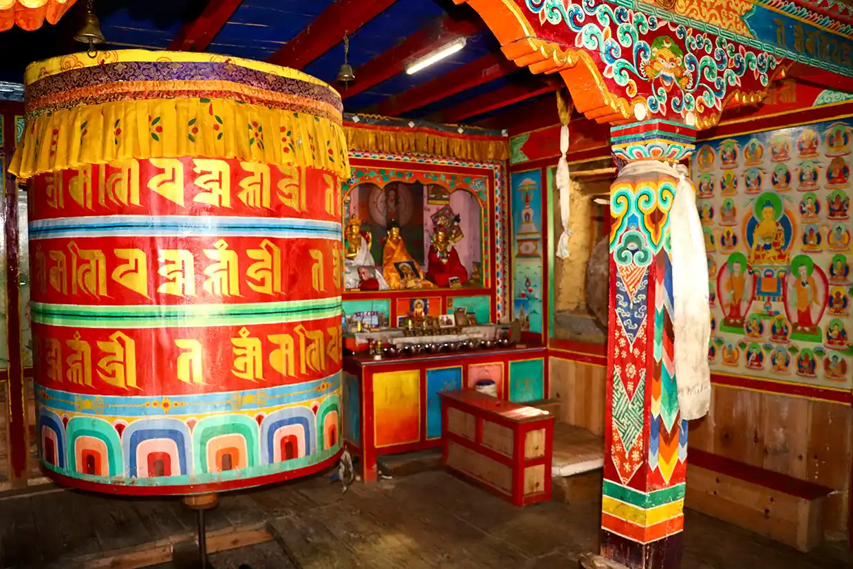A large colorful Buddhist prayer wheel stands inside a decorated shrine at mu gompa.webp along the remote Manaslu Tsum Valley Trek trail.