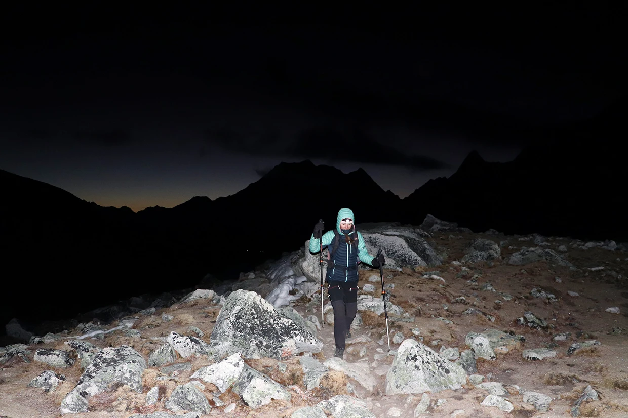 A hiker wearing a headlamp and warm jacket walks on a rocky path at dawn during the high-altitude Manaslu Tsum Valley Trek.